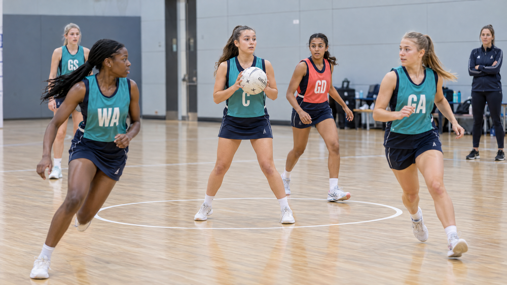 Youth netball players practising a centre pass with split attacking leads.