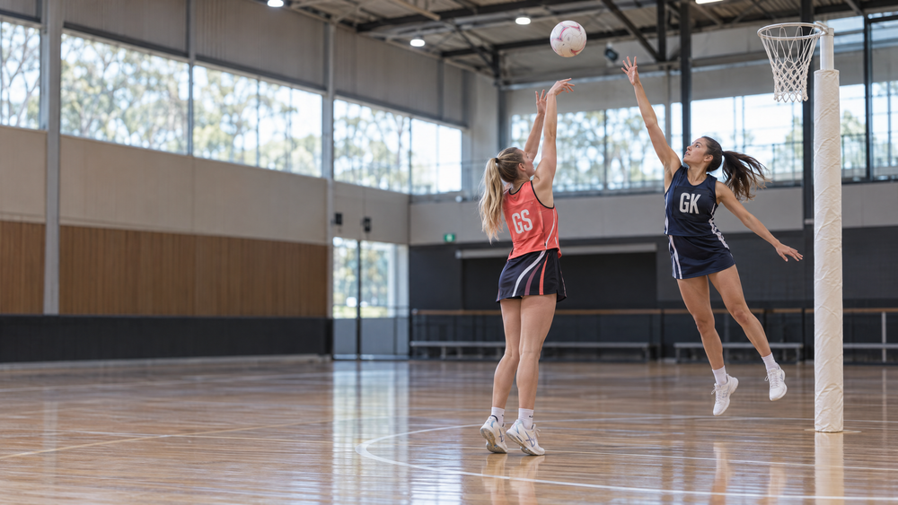 A netball goalkeeper contests a shooter’s release during indoor training